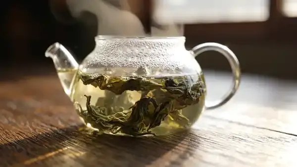 Green tea leaves slowly unfurling in a clear glass teapot as the water turns pale green