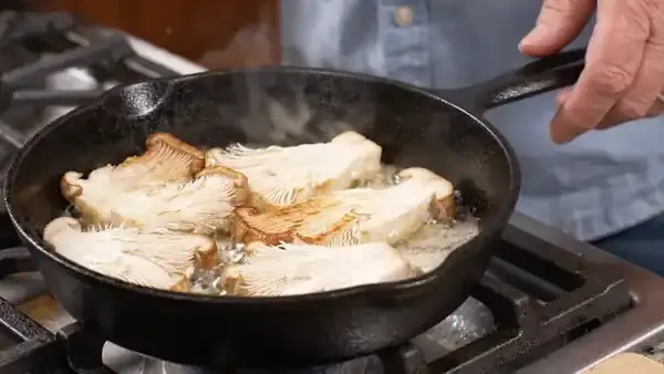Thick slices of lion's mane mushroom browning in butter in a black cast-iron pan