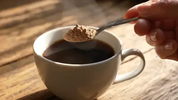 Pale powder swirling into black coffee in a white cup as a spoon stirs it in