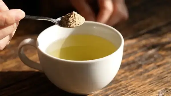Green tea turning slightly cloudy as a spoonful of pale powder is stirred into the cup